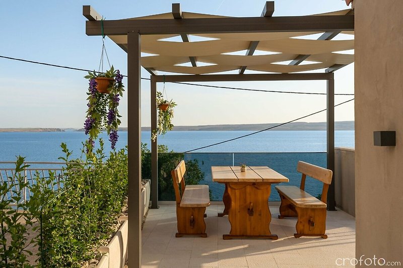 A charming lakeside cottage with a wooden pergola and outdoor furniture.