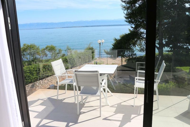 Haus am See mit Terrasse, Gartenmöbeln und herrlichem Blick auf das Wasser.