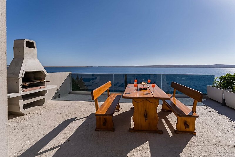 A relaxing outdoor setting with a wooden table, chairs, and a view of the ocean.