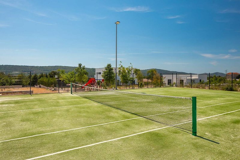 A picturesque sports venue with a tennis court and lush green grass.