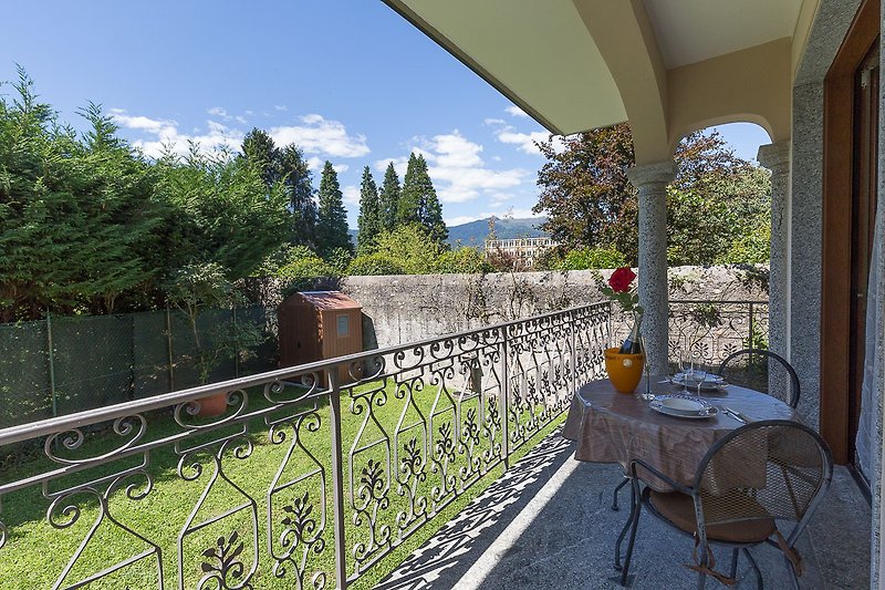 Die überdachte Terrasse ist mit Tisch und Stühlen ausgestattet und bietet Blick auf den Garten und die Berge.