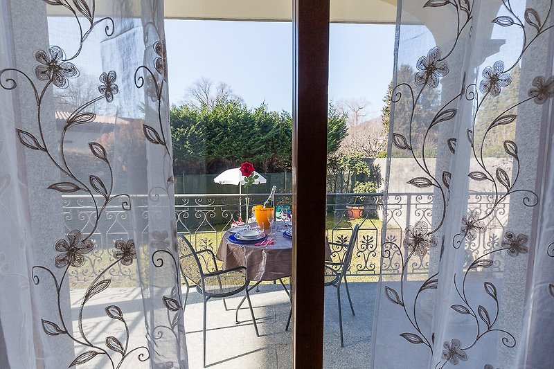Blick vom Wohnzimmer auf die überdachte Terrasse und den Garten der Petite Dame am Lago Maggiore.