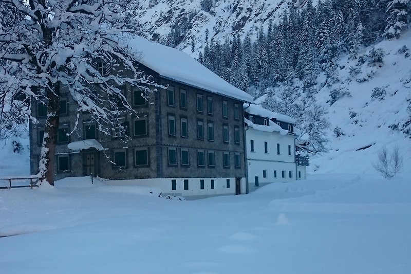 Winterliches Haus mit verschneitem Dach, umgeben von majestätischen Bergen. - Bad Rothenbrunnen