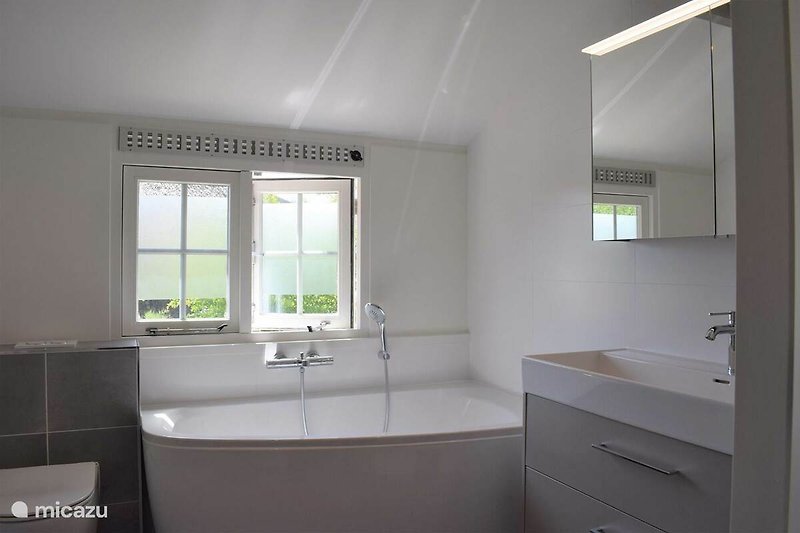 Schönes Badezimmer mit Spiegel, Badewanne und Holzboden.