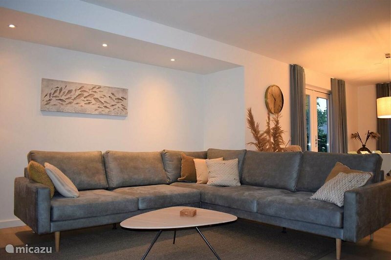 Gemütliches Wohnzimmer mit braunem Sofa, Tisch und Pflanzen. Moderne Inneneinrichtung mit Holzboden und Kunstwerk.