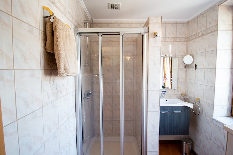 Salle de bain moderne avec douche en verre, robinetterie et carrelage.
