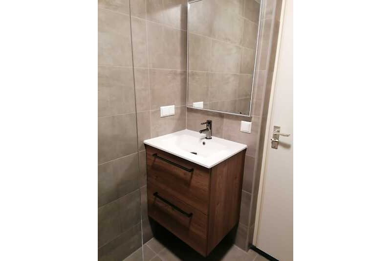 Moderne badkamer met spiegel, wastafel en kasten.
