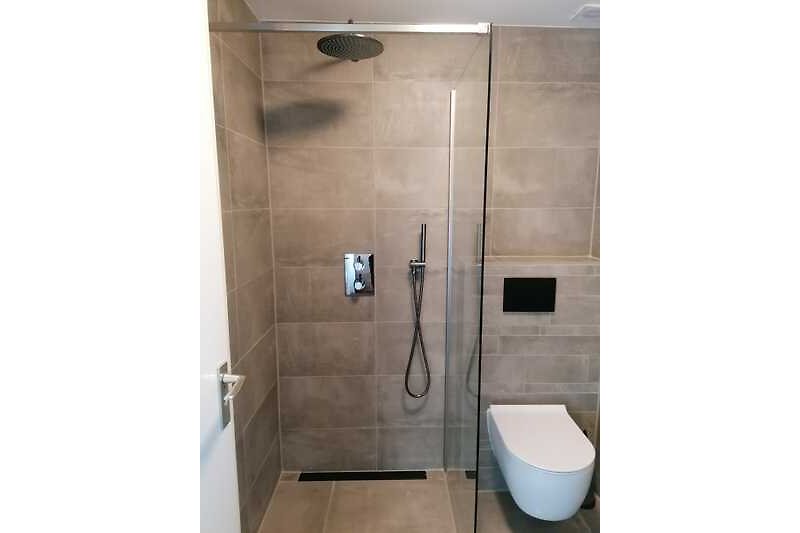 Moderne badkamer met douche, glazen deur en keramische tegels.