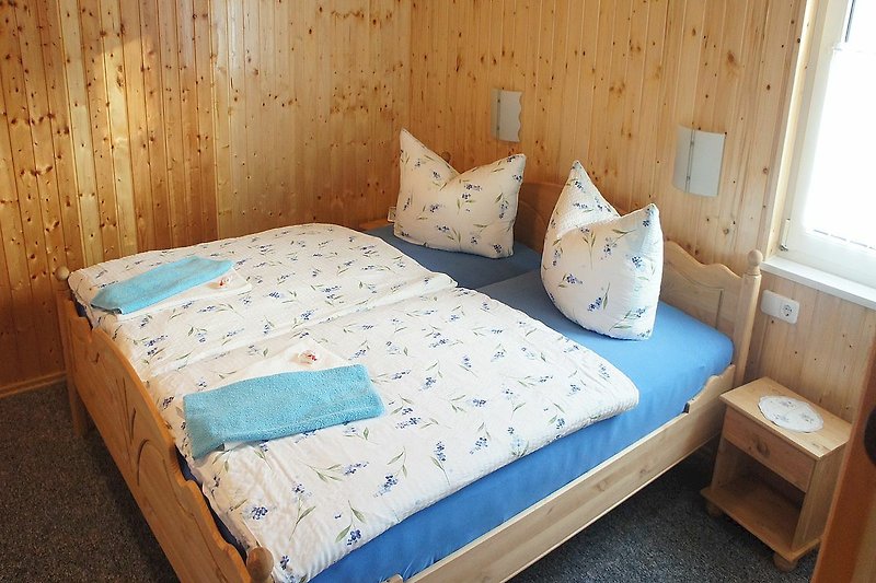 Gemütliches Schlafzimmer mit Holzbett, Fenster und Bettwäsche