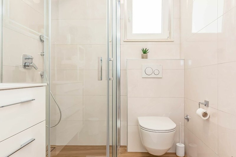 Udobna kupaonica s modernim tušem i staklenim vratima.