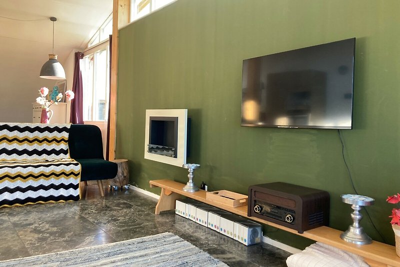 Wohnzimmer mit Fernseher, Couch, Tisch und Lampe.