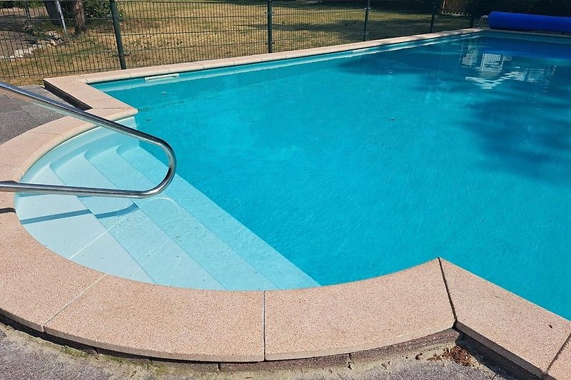 Een rechthoekig zwembad met blauw water en een betegeld terras.