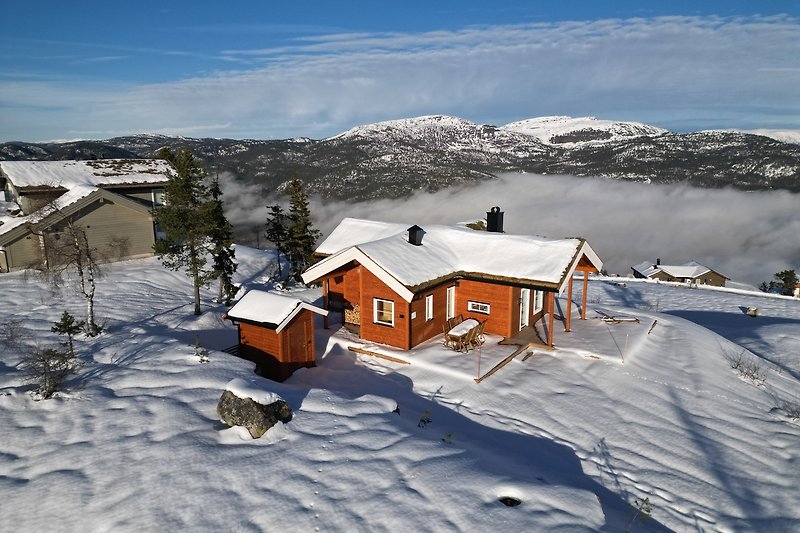Berglandschaft mit verschneitem Haus und winterlichem Himmel.