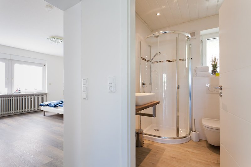 Modernes Badezimmer mit Dusche, Fenster, Holzboden und Glasdetails.