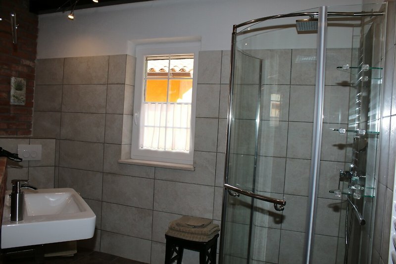 Ein modernes Badezimmer mit Dusche, Waschbecken und Fenster.