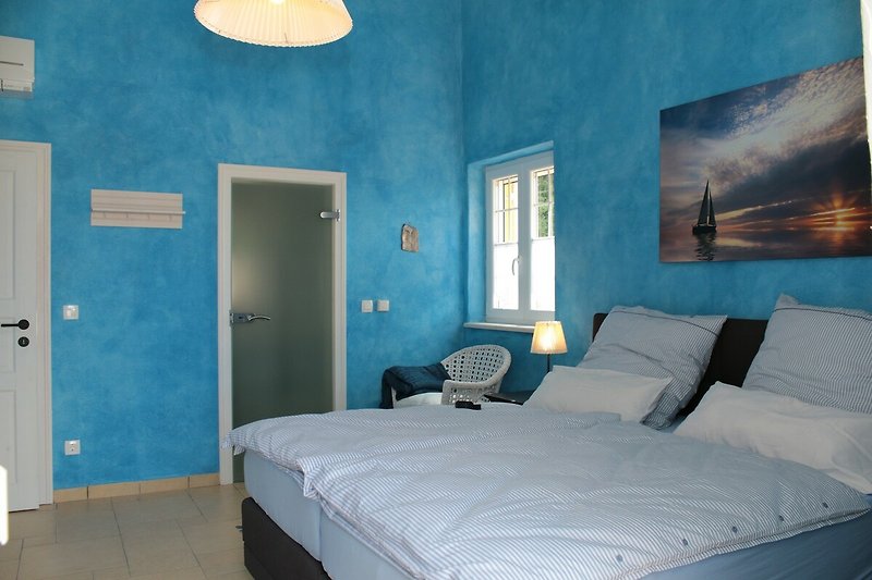 blaues Schlafzimmer mit Boxspringbetten - Glastüre zum Badezimmer