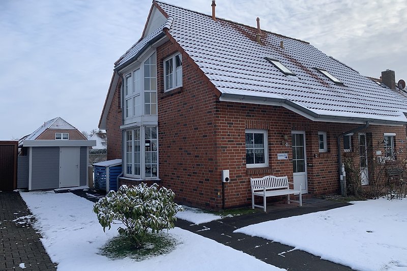 Ein winterliches Haus mit Schnee, Kamin und großem Vorgarten mit Sitzgelegenheit
