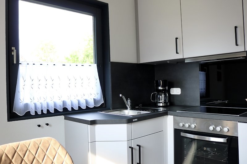 Moderne Küche mit weißen Schränken, Holzboden und Fenster.