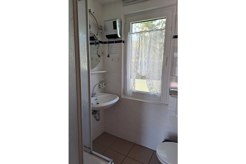 Badezimmer mit Fenster, Spiegel und Waschbecken.
