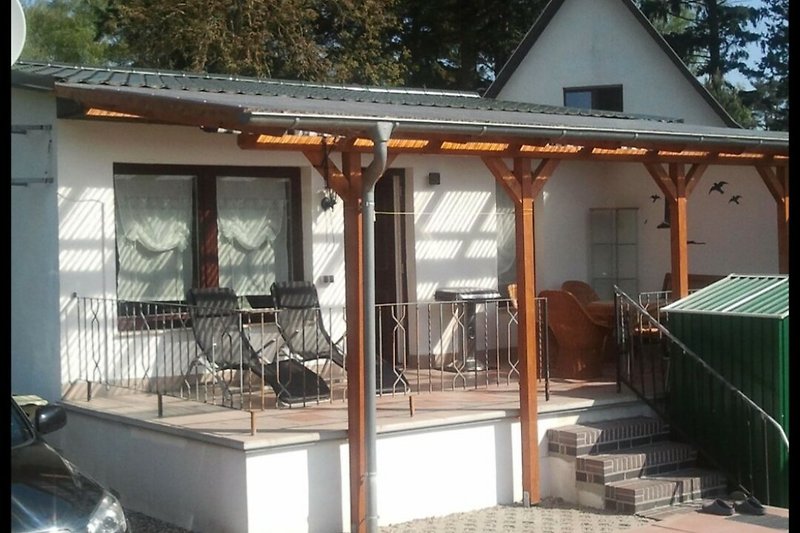 Holzmöbel auf überdachter Terrasse mit Blick auf Garten.
