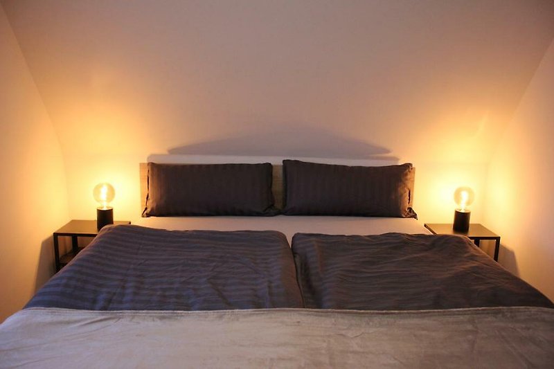 Gemütliches Schlafzimmer mit Holzbett, Lampenschirm und gemütlicher Bettwäsche.