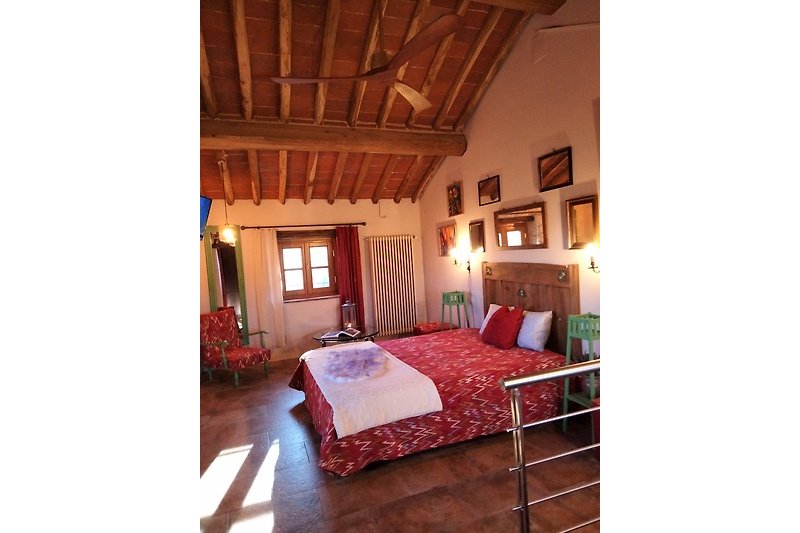 Gemütliches Schlafzimmer mit stilvoller Beleuchtung , bequemem Bett, grossen Deckenventilator aus Holz und Sitzecke