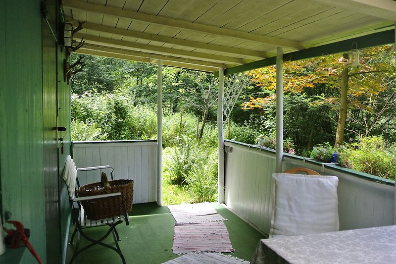 überdachte Terrasse mit Tisch Stühlen, Blick auf Wiese, dies ist auch der Eingangsbereich worüber man die Hütte betritt.