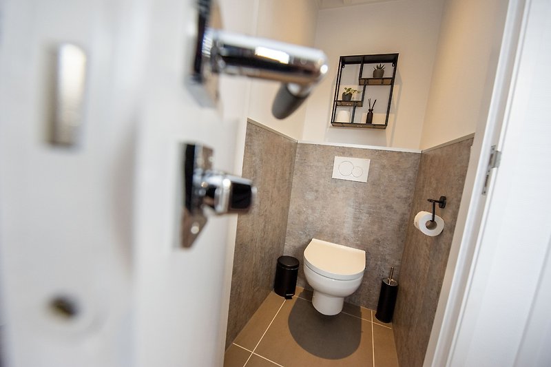 Een moderne badkamer met toilet, wastafel en papierhouder.