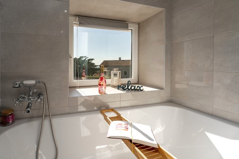 A modern bathroom with a bathtub, wood flooring, and glass fixtures.