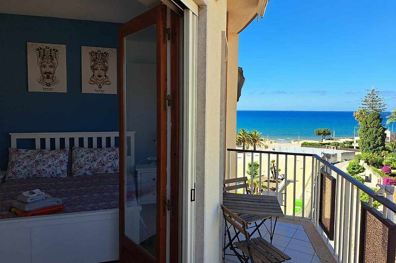 Strandvilla mit Balkon, Holzveranda, Meerblick und tropischen Pflanzen.