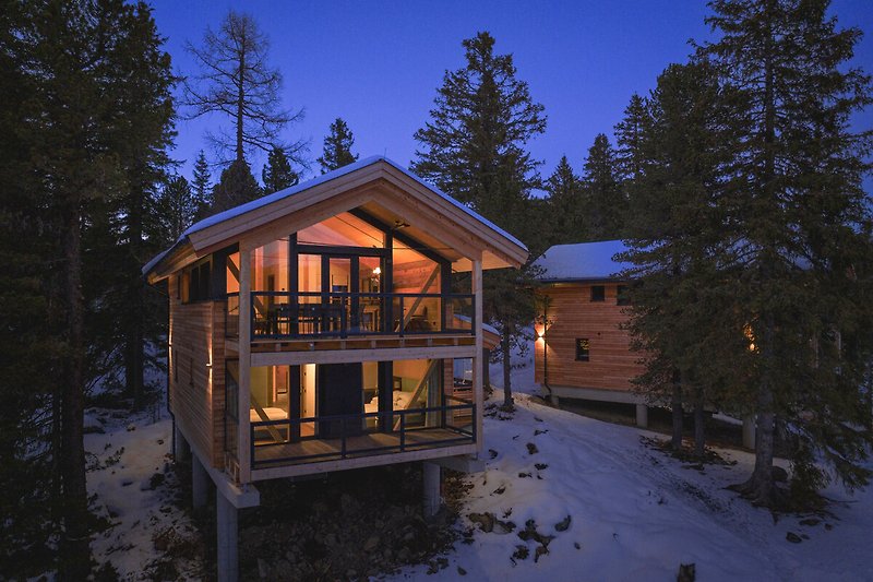 Prachtige houten cottage met besneeuwd dak en uitzicht op de bergen bij zonsondergang.
