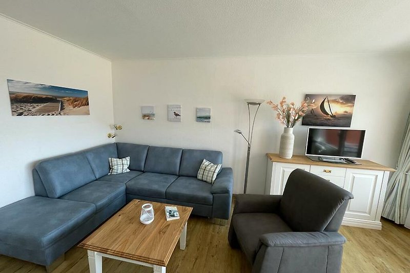 Gemütliches Wohnzimmer mit Couch, Tisch und Sessel. Sideboard mit Fernseher.