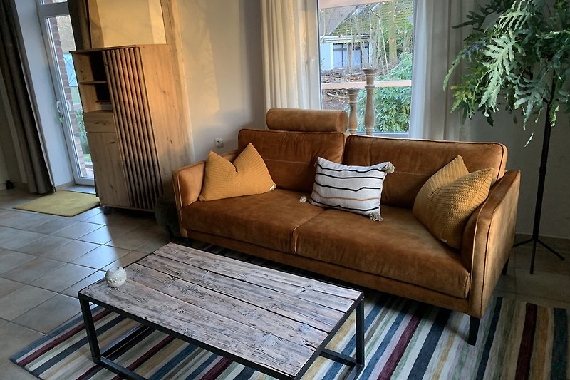 Gemütliches Wohnzimmer mit bequemer Couch und großen Fenstern. Mit Zugang übedachte Terrasse