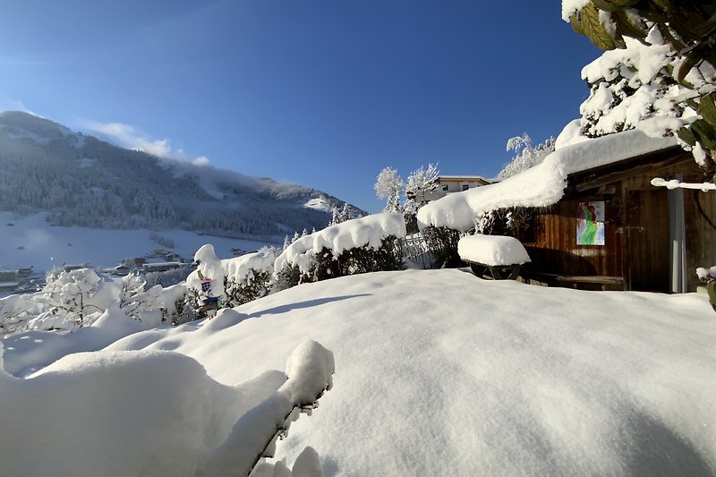 Ein winterliches Bergpanorama mit schneebedeckten Gipfeln und dem Saunahäuschen