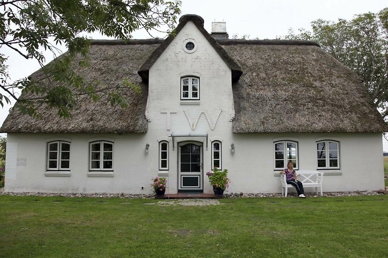 Schönes Bild von einem Haus mit thatched Dach, umgeben von grüner Landschaft und Bäumen. Perfekt für Naturliebhaber.