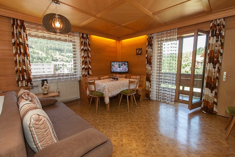 Gemütliches Wohnzimmer mit Holzmöbeln und großen Fenstern.