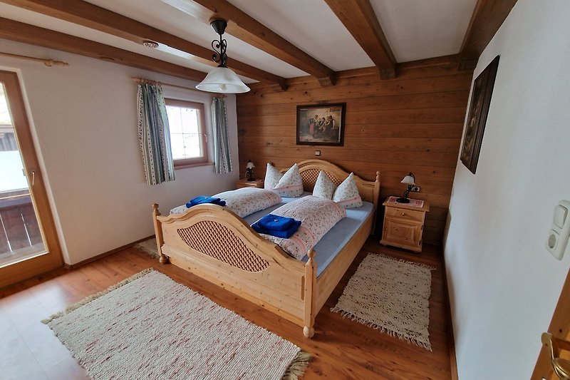 Gemütliches Schlafzimmer mit Holzbalken, großen Fenstern und stilvollem Interieur.