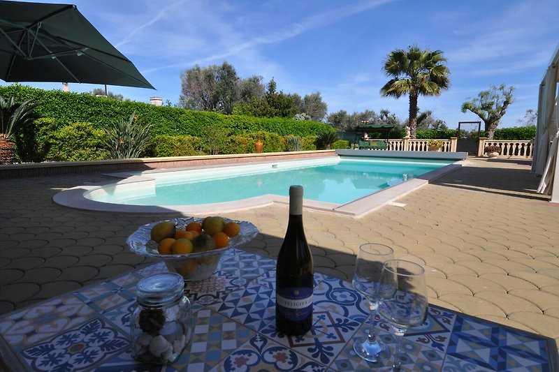 Sommerlicher Poolbereich mit Sonnenschirm, Glasflasche und Wein.