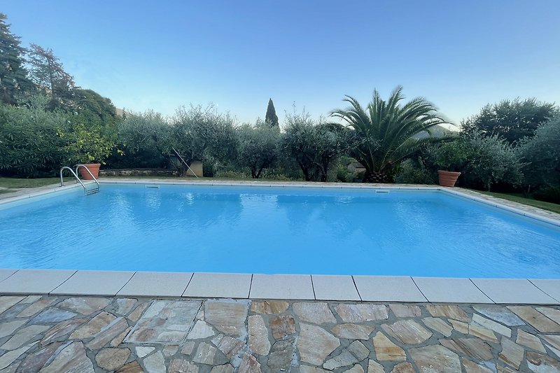 Schwimmbad mit azurblauem Wasser, umgeben von grüner Landschaft und einem modernen Gebäude.