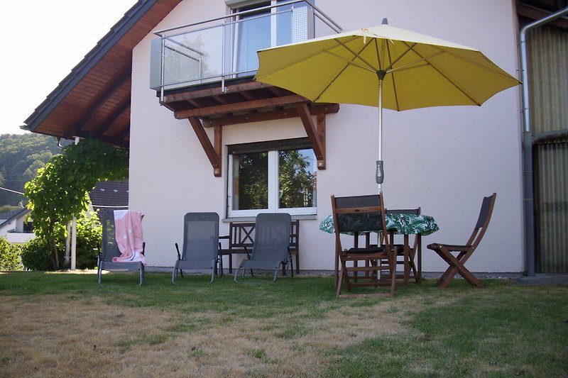 Ferienhaus mit Möbeln, Tisch, Stühlen und Sonnenschirm im Freien.