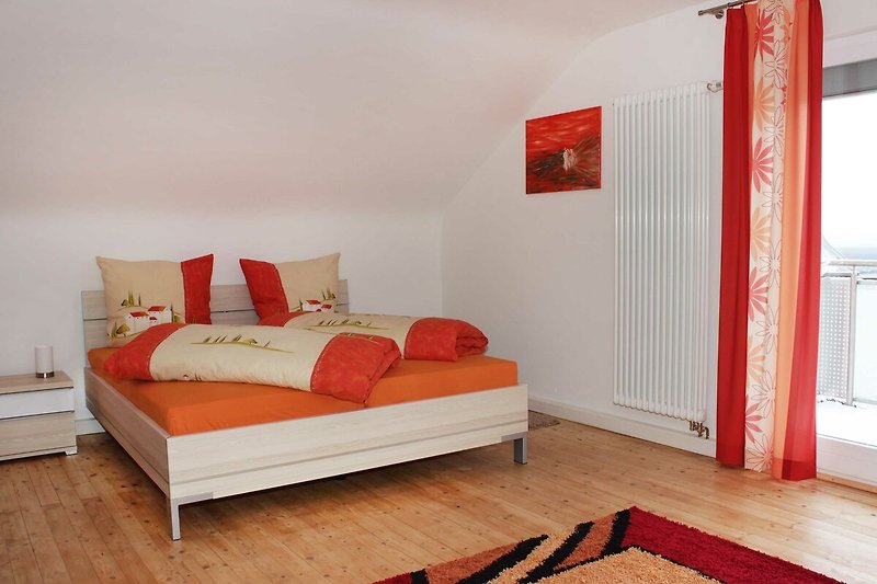 Gemütliches Schlafzimmer mit Holzbett, roten Kissen und orangefarbenem Lampenschirm.
