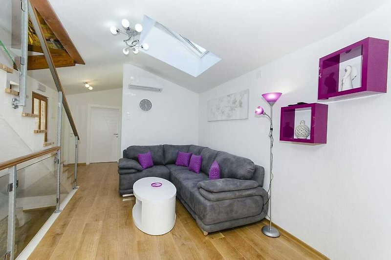 Gemütliches Wohnzimmer mit lila Couch und Holzboden.