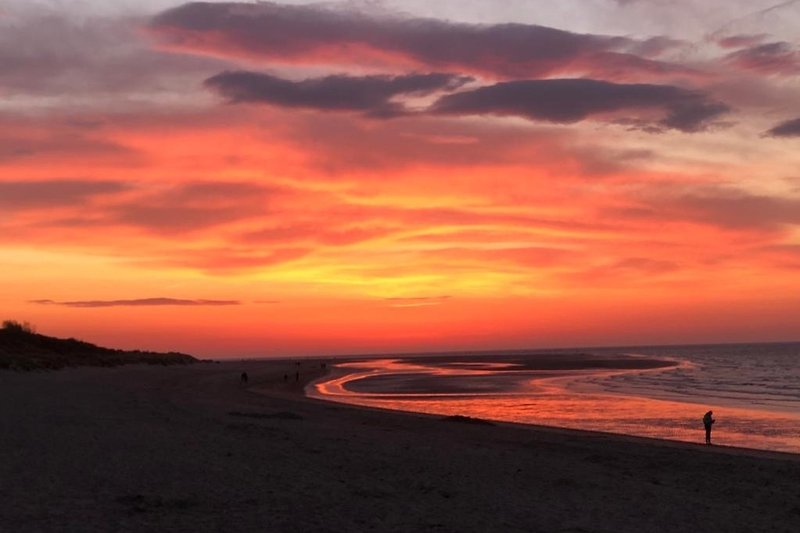 Ruhiger Strand mit rotem Sonnenuntergang über dem Ozean.