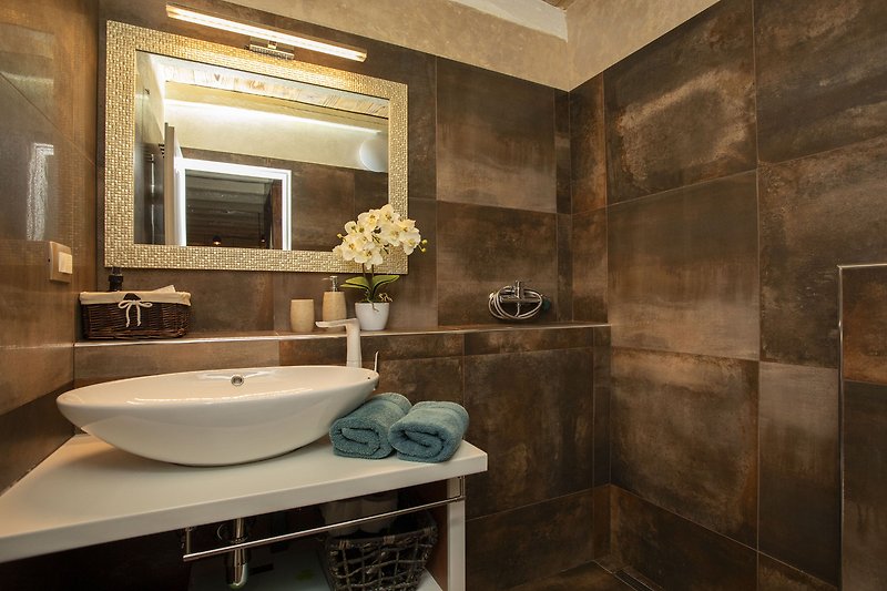 Elegantna kupaonica s ogledalom, umivaonikom i modernim osvjetljenjem.