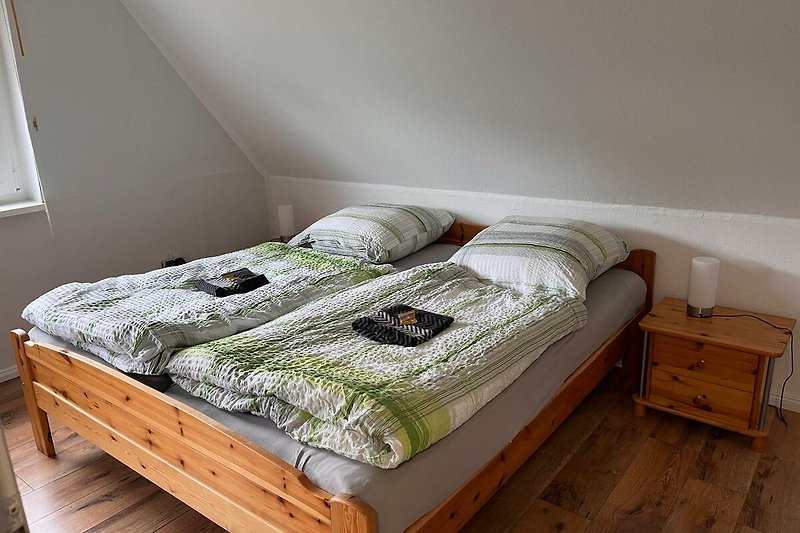 Gemütliches Schlafzimmer mit Holzbett, Bettwäsche und Kunst an der Wand.