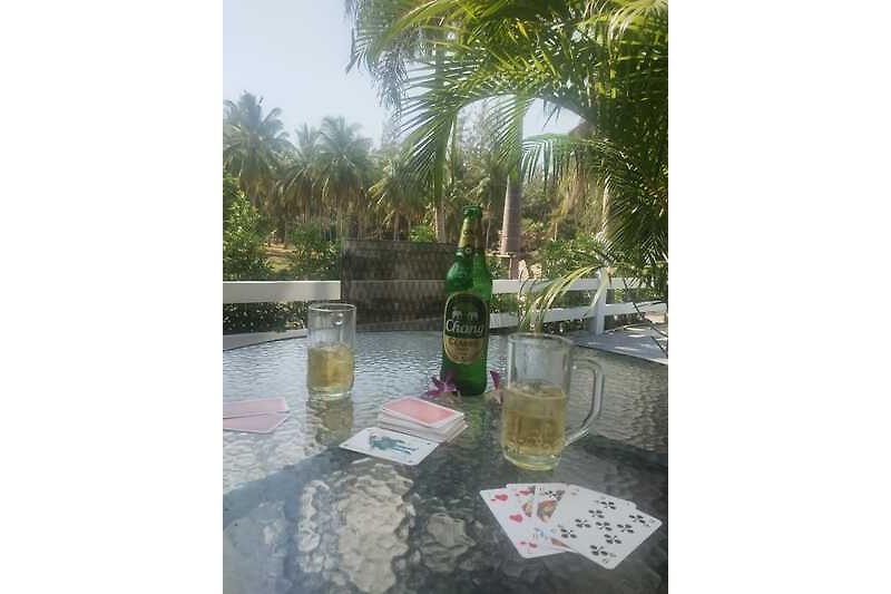 Eine entspannte Atmosphäre mit Tisch, Stühlen und erfrischenden Getränken unter Palmen.