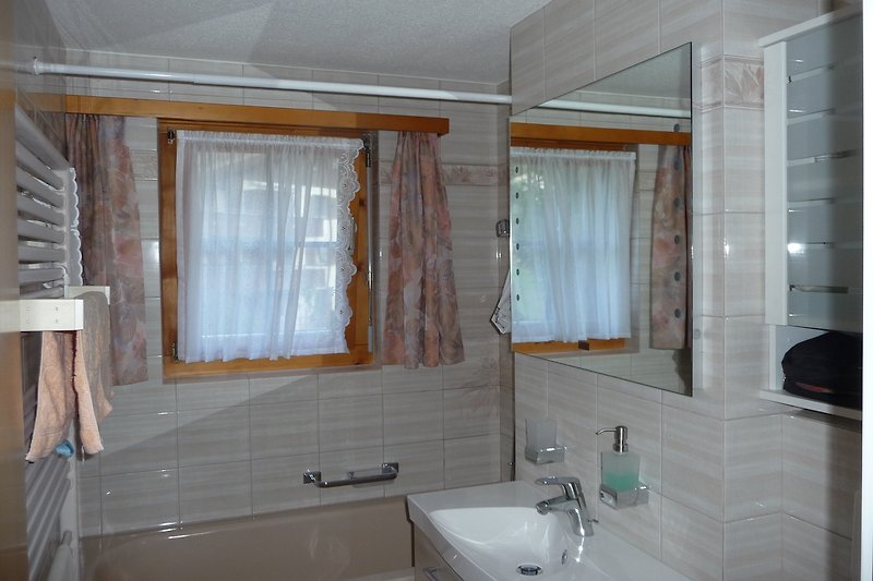 Badezimmer mit Spiegel, Waschbecken, Wannenbad/ Dusche, Handtuchheizung, hochwertige Wand-/Bodenfliesen.
