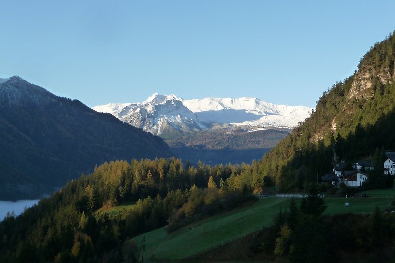 Berglandschaft mit schneebedeckten Gipfeln und grünen Wiesen.