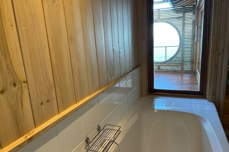 Stylish bathroom with a bathtub, hardwood flooring, and a beautiful window treatment.
