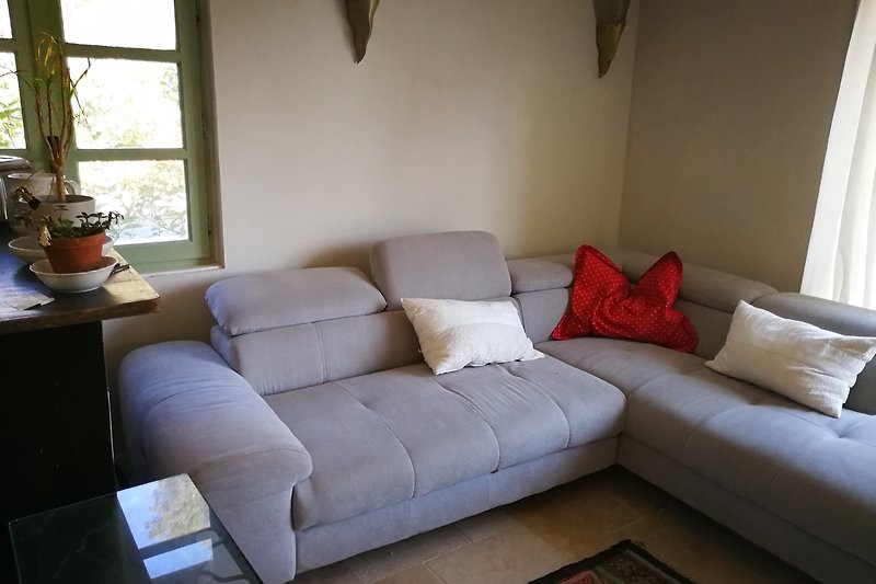 Gemütliches Wohnzimmer mit hellgrauer Couch, Holzmöbeln und grauem Dekor.